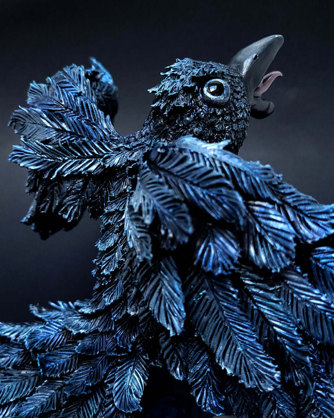 Sculpture d'un corbeau noir irisé bleu, ailes déployées, gardant une citrouille sous ses serres.
