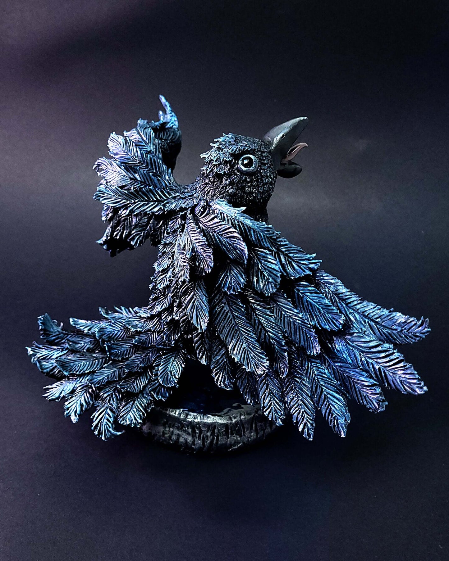 Sculpture d'un corbeau noir irisé bleu, ailes déployées, gardant une citrouille sous ses serres.