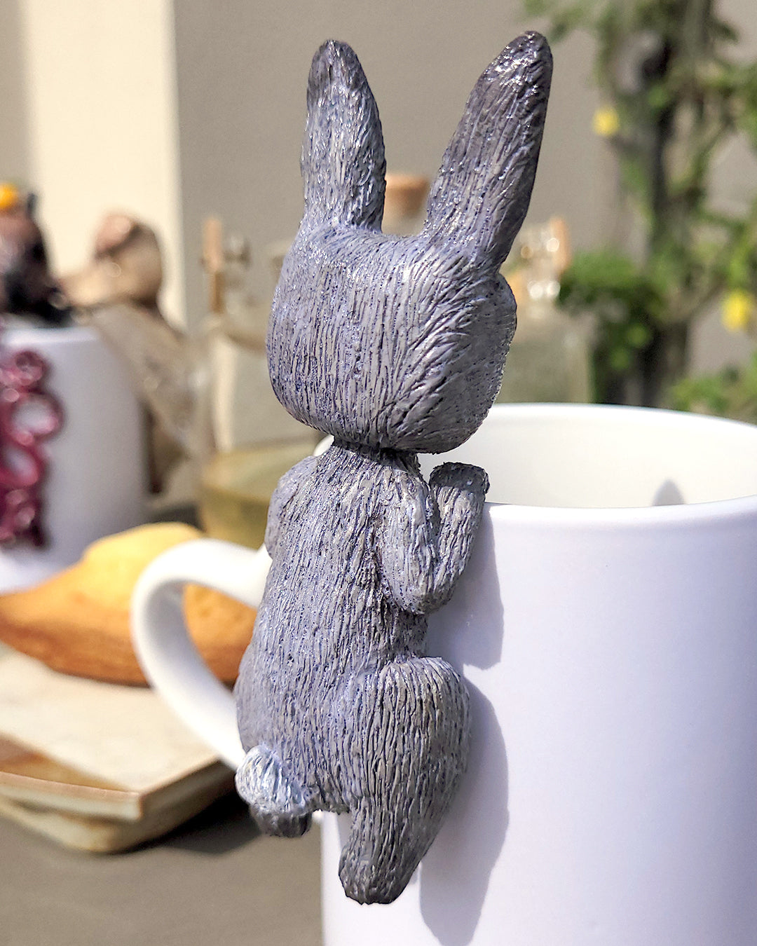 Mini figurine en forme de lapin gris accrochée à une tasse de thé vert, accompagné de madeleines