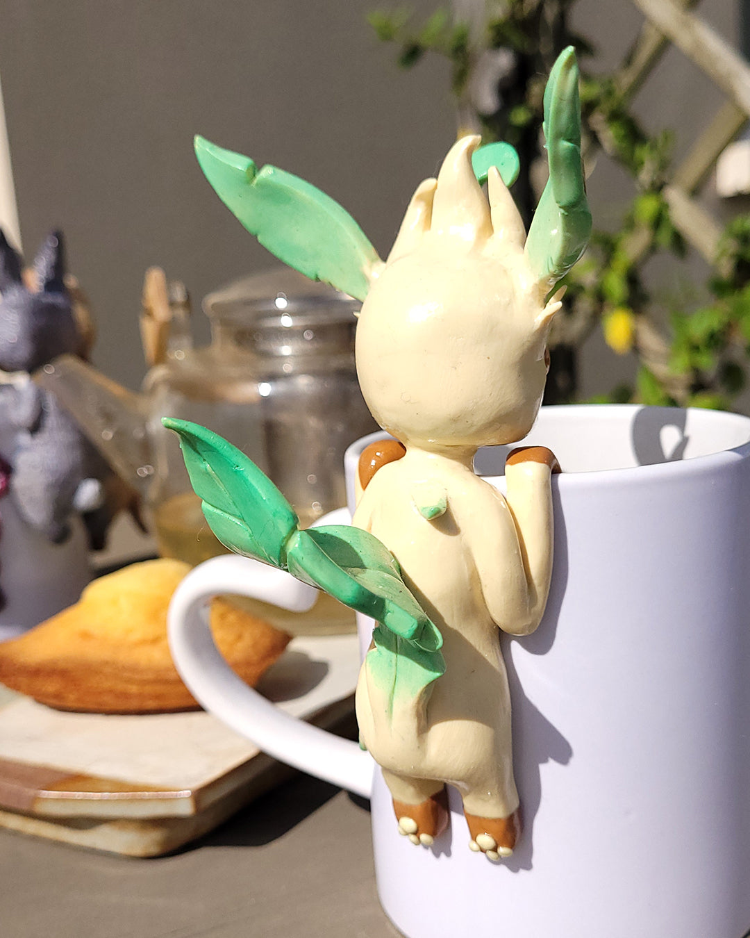 Mini figurine en forme de Phyllali accrochée à une tasse de thé vert, accompagné de madeleines