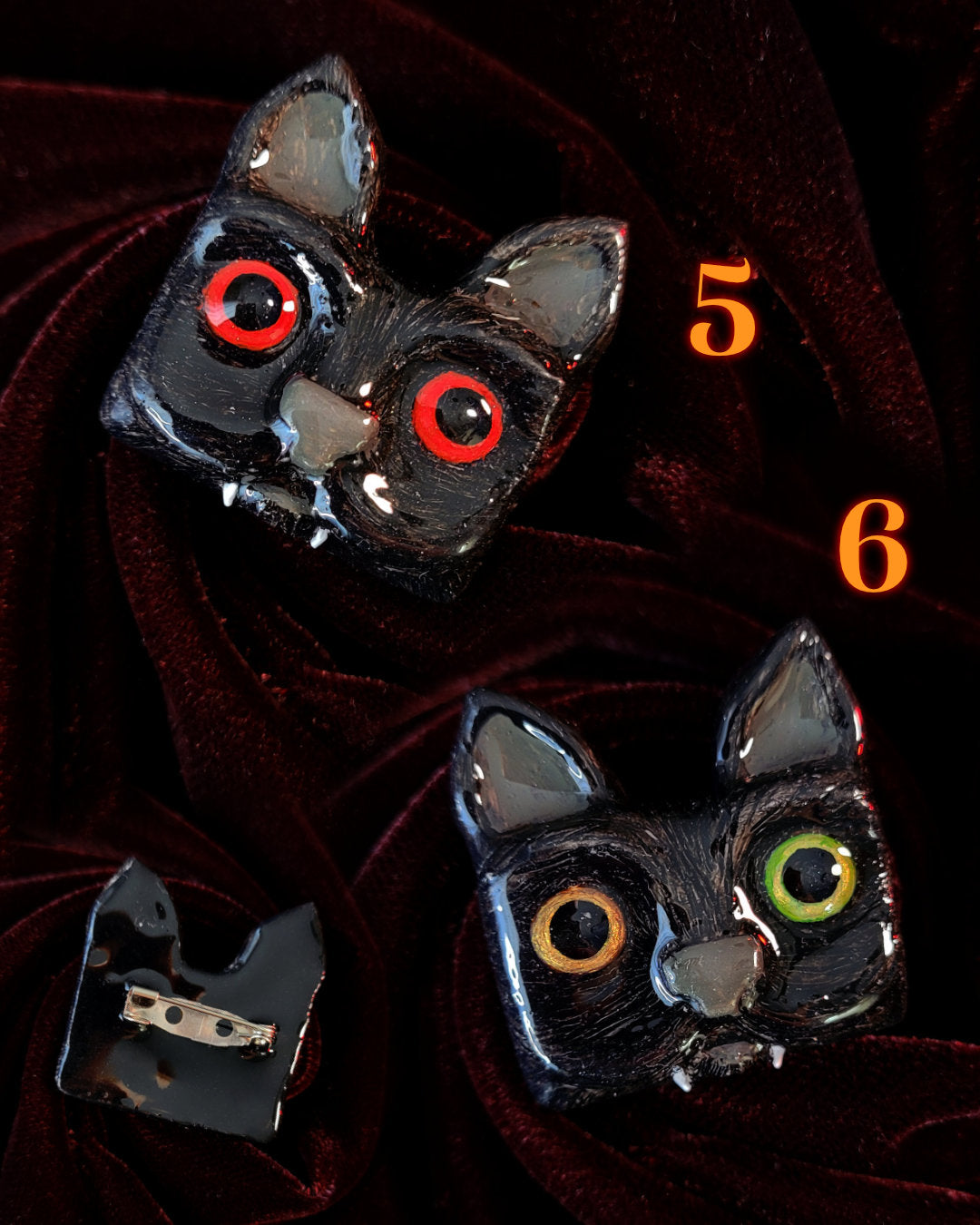 Duo de broches faites main en forme de chats noirs avec des dents de vampire. L'un a les yeux rouges, l'autres des yeux hétérochromes vert et doré.