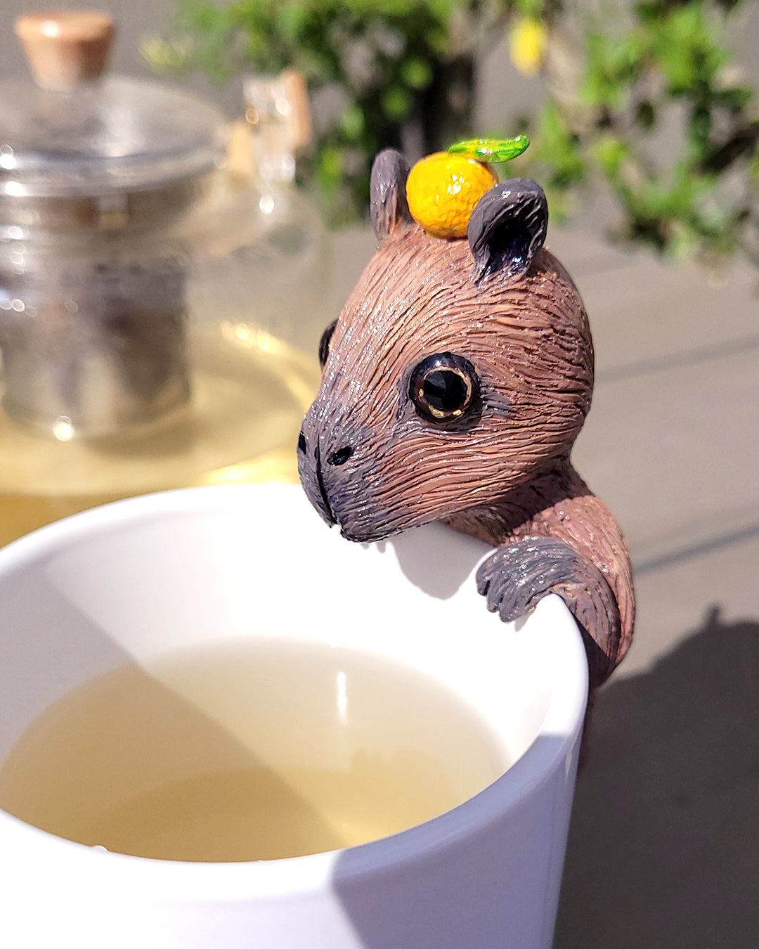 Mini figurine en forme de capybara avec un yuzu sur la tête accrochée à une tasse de thé vert