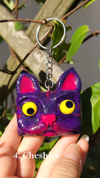  Porte clef en forme de tête de chat violet et fuchsia aux yeux jaunes qui louchent inspiré du Cheshire