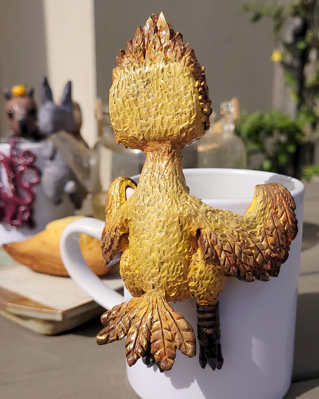  Mini figurine en forme d'oiseau doré type Chocobo accrochée à une tasse de thé vert, accompagnée de madeleines