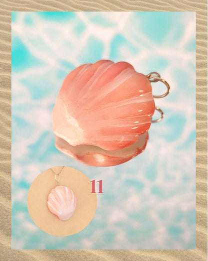 Pendentif irisé rose corail en forme de coquillage, sur un fond aquatique faisant penser à la surface d'une piscine et encadré de sable.