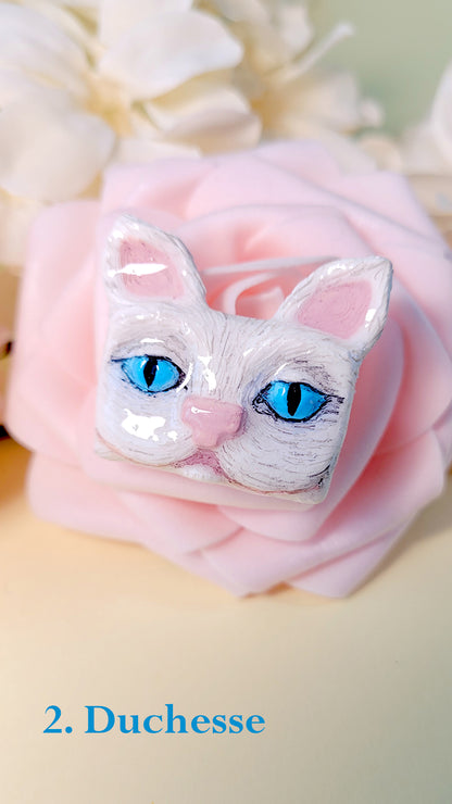 Pins en forme de tête de chat blanc aux yeux bleus, sur une rose