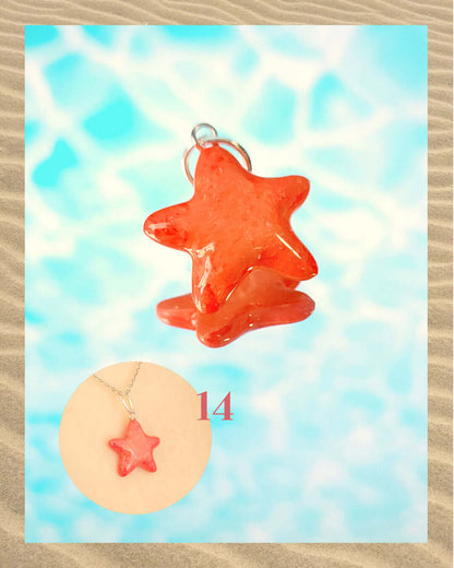 Pendentif rouge corail en forme d'étoile de mer, sur un fond aquatique faisant penser à la surface d'une piscine et encadré de sable.