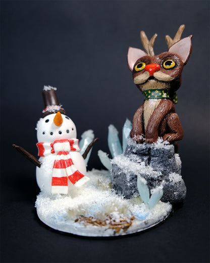 Figurine mignonne sur le thème de l'hiver avec un chat renne et un bonhomme de neige dans un environnement montagnard