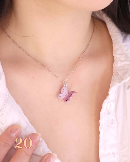 Pendentif en forme de papillon rose porté au cou d'une femme grâce à une chaînette