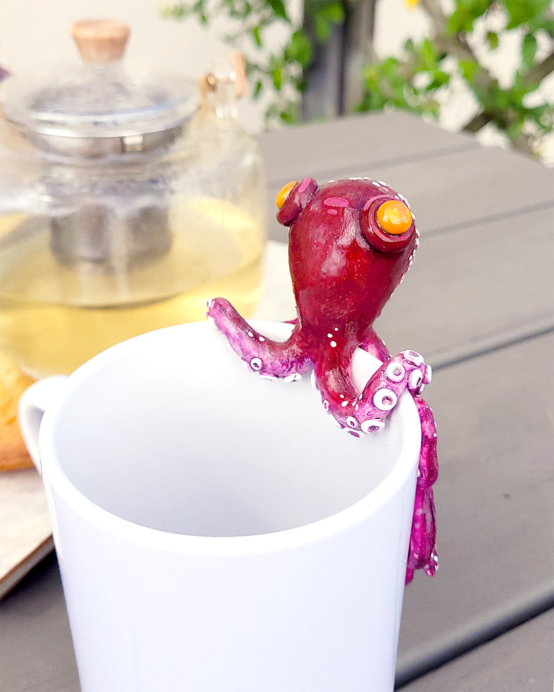 Mini figurine en forme de poulpe violet aux yeux oranges accrochée à une tasse de thé vert