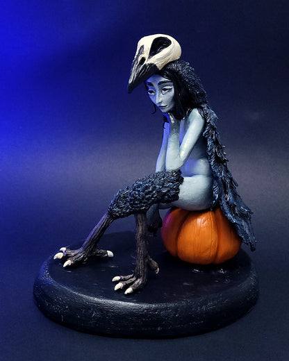 Sculpture fantasy d'une harpie mi-femme mi-corbeau assise sur une citrouille