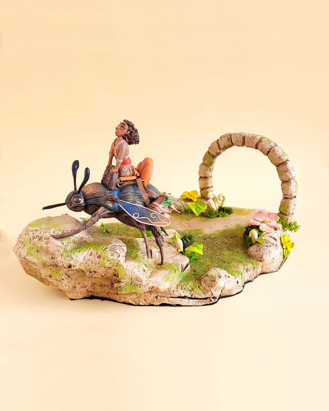 Diorama mettant en valeur une sculpture de machine scarabée géante montée par un personnage féminin. Le décors est riche en verdure.