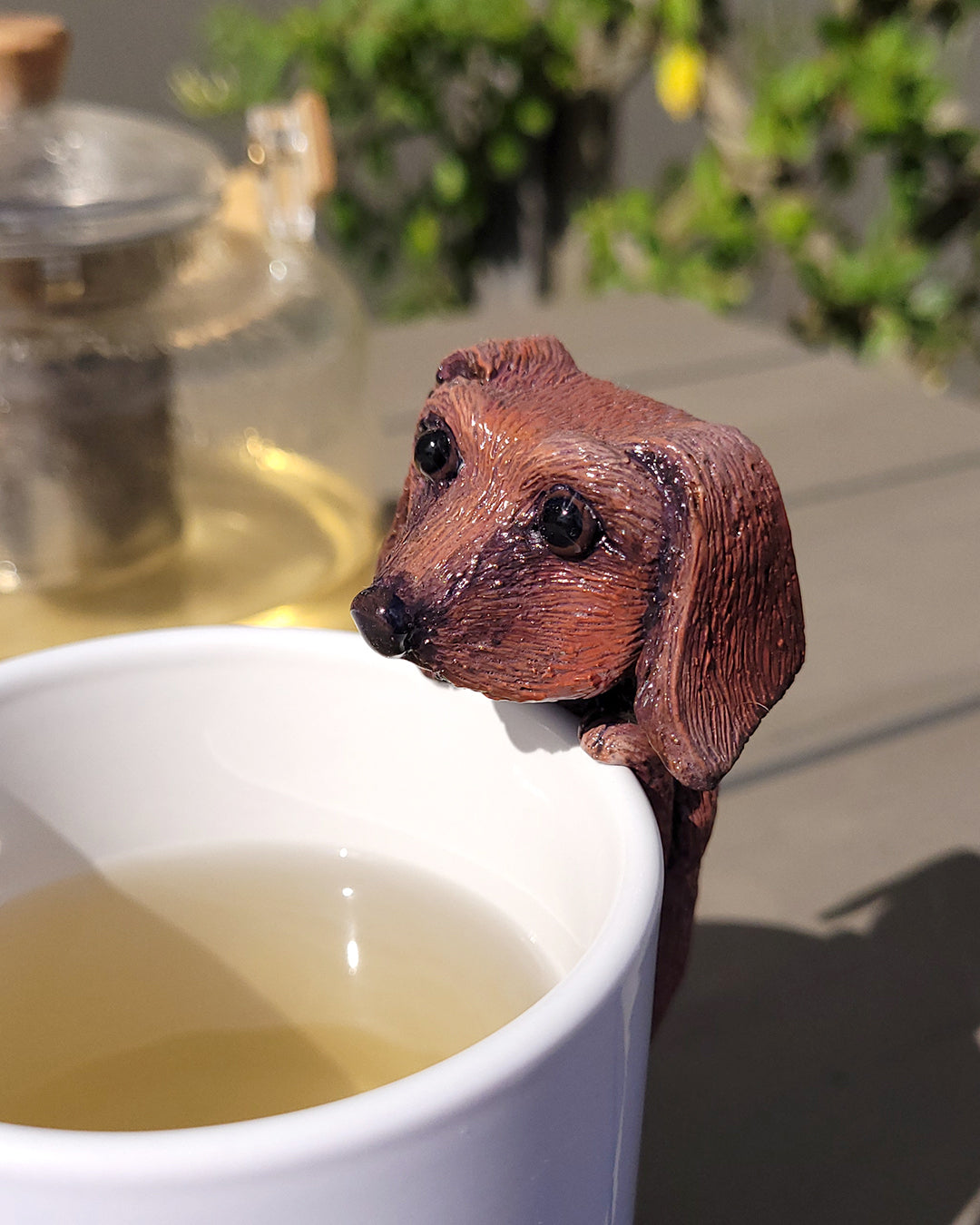 Mini figurine en forme de teckel accrochée à une tasse de thé vert