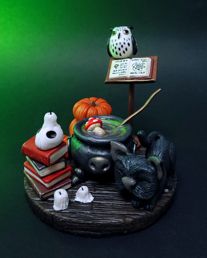 Diorama d'un atelier de potions avec un chaudron, des grimoires, un hibou, un chat noir