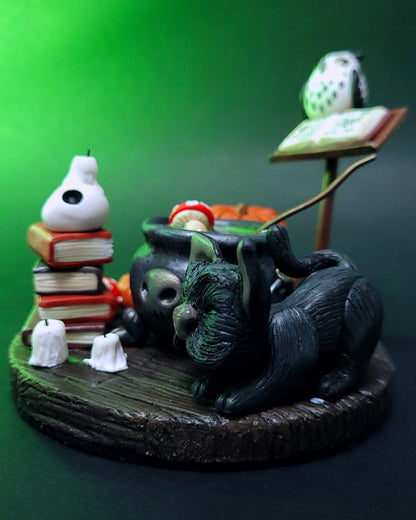 Diorama d'un atelier de potions avec un chaudron, des grimoires, un hibou, un chat noir