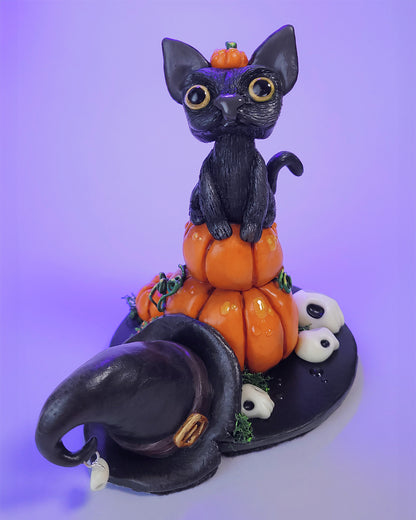 Figurine mignonne sur le thème d'Halloween et de l'automne avec un chat noir sur des citrouilles, avec un chapeau de sorcière et des crânes phosphorescents